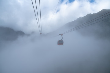 The cable car to mountain top with low clouds and mountain view