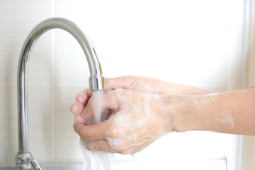 Hands of woman wash their hands in a sink with foam to wash the skin and water flows through the hands. Concept of health, cleaning and preventing germs and coronavirus from contacting hands