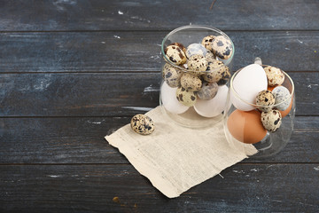 Quail eggs and white and yellow eggs of chicken in a glass container on wooden background.