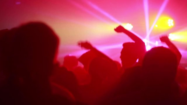 Crowd dances in front of multicolored lights.