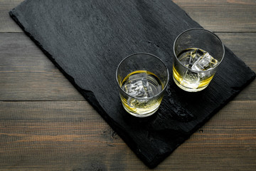 In the bar. Whiskey with ice on black desk on wooden background top view space for text