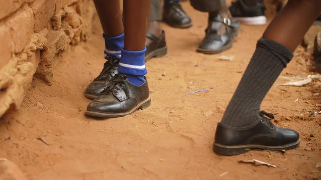 Rural African school pupils' shoes in the soil as they step forward in a line