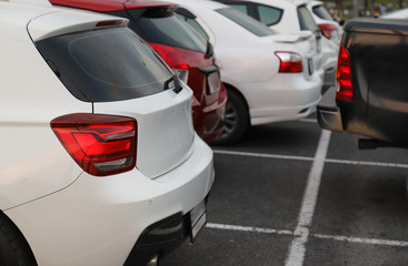 Closeup of back or rear side of white car and other cars parking in parking area in the evening of sunny day. 