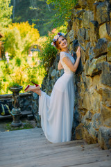 a young sexy bride with circlet of flowers posing and smiling standing on wooden stairs near rock fence