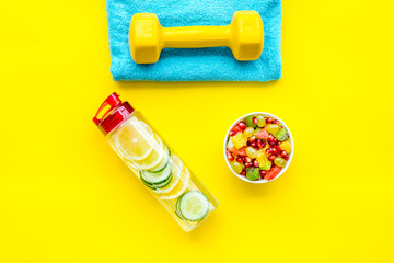 Healthy lifestyle, healthy habits. Detox water, fruit salad, sport equipment dumbbells on yellow background top view copy space
