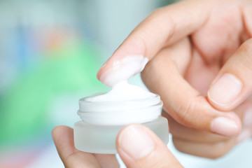 Hand of woman holding moisturizer cream and serum. She applying a facial cream , essential , oil , lotion and body cream for skin care, close up view and blur background. Beauty and Healthy Concept.