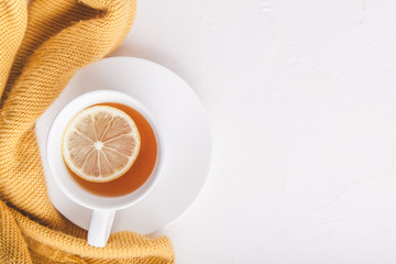 White cup of tea with lemon on a saucer on white background with a cozy orange sweater. Copy space. Flat lay