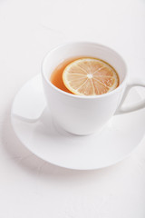 White cup with saucer with tea and lemon on white background. Copy space
