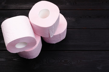 Pastel pink toilet paper rolls on black wooden background