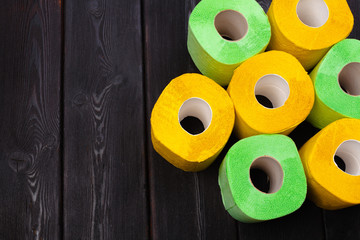 Green and yellow toilet paper rolls on dark wooden background top view