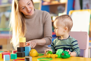 Obraz premium Cute nursery teacher and child toddler boy playing educational toys in kindergarten