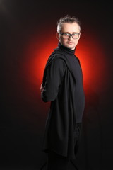 Portrait of a young man with glasses and black clothes on a black background in the studio