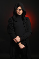 Portrait of a young man with glasses and black clothes on a black background in the studio