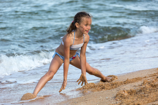 young girl athlete in a swimsuit at sea playing on the beach on the sand, legs open