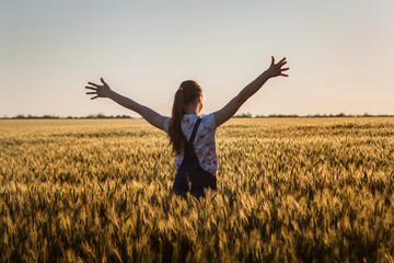 landscape, a huge wheat field in the middle of summer, a girl with long hair opened her arms to sunset