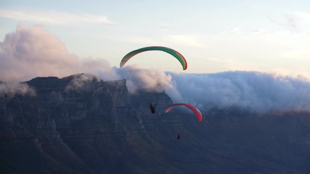 Two paragliders flying next to each other on the coastline at dusk