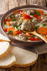 Delicious Italian soup with orzo pasta, meatballs and vegetables close-up on the table. vertical, rustic