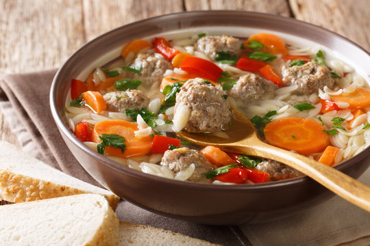 Italian soup with pasta orzo, meatballs and vegetables close-up in a plate served with bread. horizontal