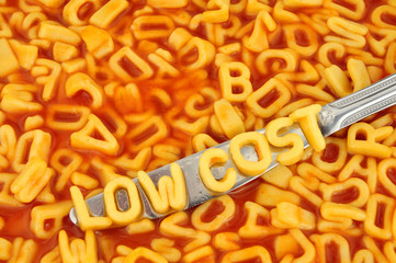 Alphabet spaghetti spelling low cost with random letters in tomato sauce background