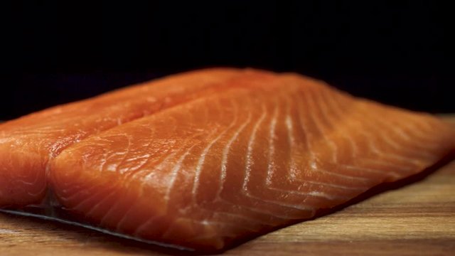 Close-up of juicy piece of salmon. Juicy fresh and red slice of salmon meat lying on wooden board on black background