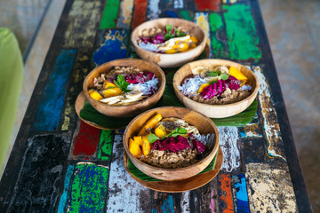 Close up four smoothies bowls made with mango, banana, granola, grated coconut, dragon fruit, chia seeds and mint on colored background
