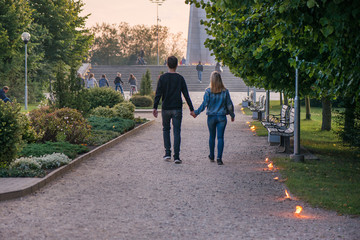 Happy couple holding hands and walking in park on lit candle path during sunset. Romantic summer evening, love is in the air. People celebrating Night of ancient lights. Calm and relaxing holidays