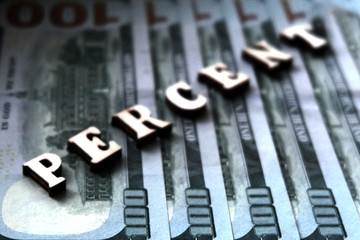 The word PERCENT is lined with wooden letters on the background of hundred-dollar bills. The concept of financial transactions and bank loans.