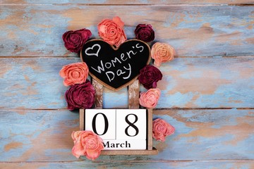 Save the date block calendar for International Womens day, March 8, with chalkboard, next to roses flowers, on blue wooden rustic background