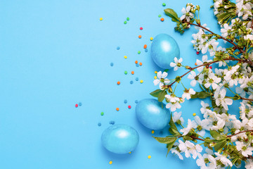 Blooming Cherry Twig, Easter Blue Eggs and Multicolored Powder on the Blue Background