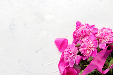 Pink peonies and pink ribbon on a light stone background. Flat lay, top view