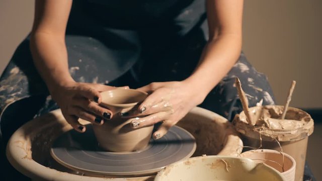 Woman girl her hands dub wall jug, sculpts out of clay on circle. Dirty hands in the clay. slow motion.