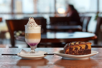 caffe mocha with whipped cream and chocolate stands on a saucer with a tube, next to a chocolate sponge cake