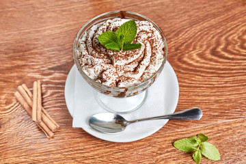 creamy dessert with chocolate chips, decorated with a sprig of mint, standing on a saucer with a napkin and a spoon, next to cinnamon and mint