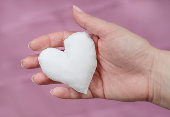 Fototapeta premium white handmade fabric heart in woman's hand in pink background