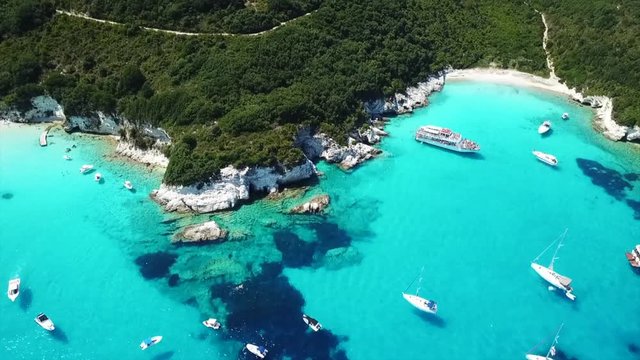 Aerial drone video of tropical paradise turquoise beach of Voutoumi with sail boats docked in island of Antipaxos, Ionian, Greece