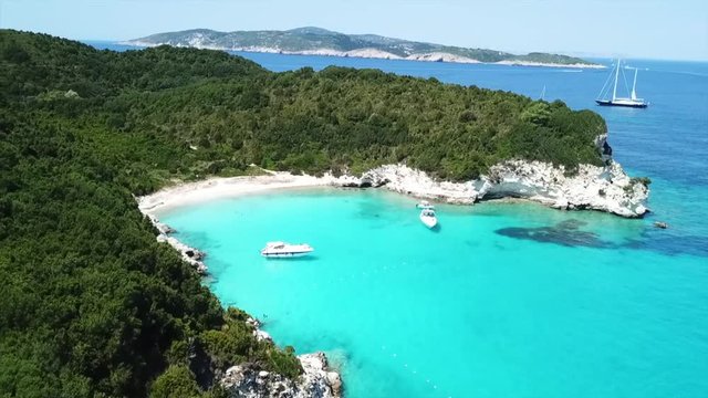 Aerial drone video of tropical paradise turquoise beach of Voutoumi with sail boats docked in island of Antipaxos, Ionian, Greece