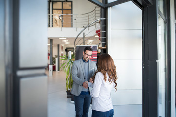 Two business people greeting at company's entrance. Corporate building interior.