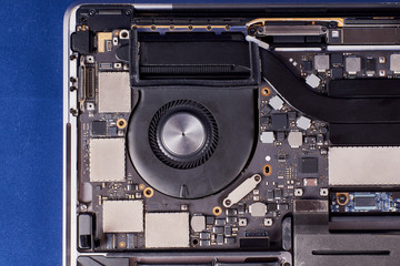Part of a disassembled laptop with a fan in an aluminum case on a blue velvet background. Close-up