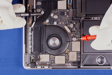 Master in the white gloves carries out diagnostics with the probes of tester. Laptop in an aluminum case on a blue velvet background. Flat lay