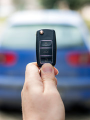 A person holding car key (remote control) in hands on blur blue car background.