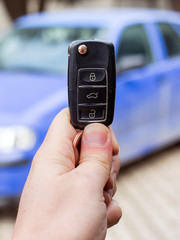 A person holding car key (remote control) in hands on blur blue car background.