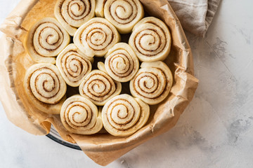 Raw cinnamon rolls in baking plate on kitchen table. Copy space.