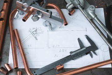 Brass pipes, pipe bender, pipe rammer tool and a layout drafts on a fitter workbench.
