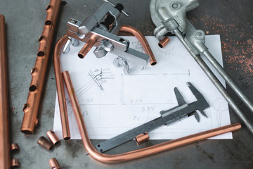 Brass pipes, pipe bender, pipe rammer tool and a layout drafts on a fitter workbench.