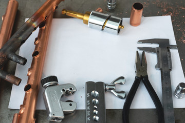 Brass pipes, pipe cutter, calipers, pliers and a blank layout drafts of pipeline system on a fitter workbench.