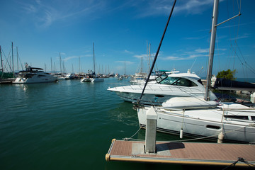 Fototapeta premium Many Luxury Yachts float on crystal clear sea in Marina Bay Club, expensive Private boat stay calm in docking pier under summer blue sky green ocean