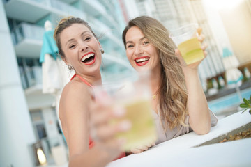 Two attractive funloving friends partying with drinks on rooftop bar in city