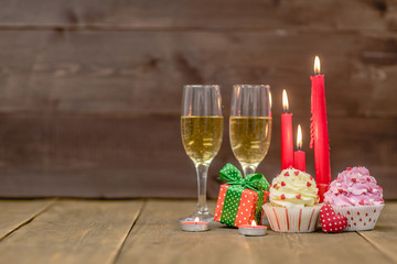 Pair glass of champagne with cupcakes, gift box and candles. Wooden background with empty space for text