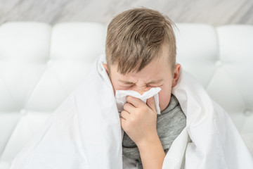 Sick child on bed and blowing his nose in tissue