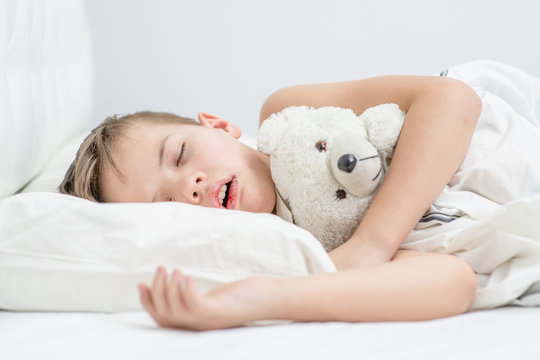 Little boy with toy bear is sleeping with his mouth open, snoring